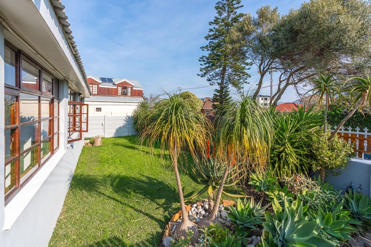 A well-maintained rear garden featuring established landscaping, a lawn area, and timber-framed windows along the side elevation of the house.