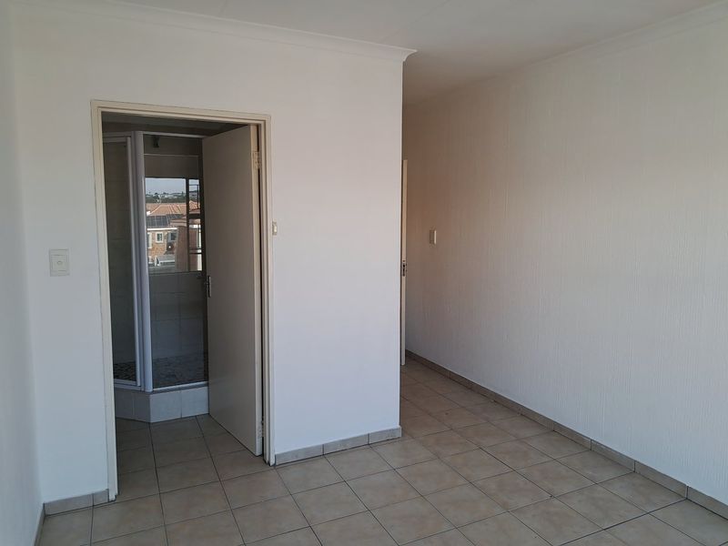 A clean, empty hallway with neutral tiled flooring and white walls, providing access to an adjacent bathroom area.