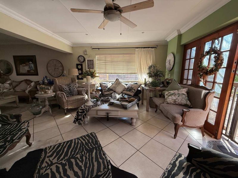 A spacious living room featuring tiled flooring, a ceiling fan, and timber-framed glass doors providing natural light and access to the exterior.