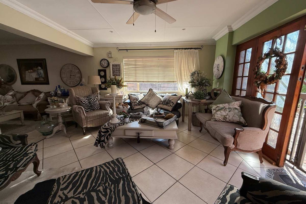 A spacious living room featuring tiled flooring, a ceiling fan, and timber-framed glass doors providing natural light and access to the exterior.