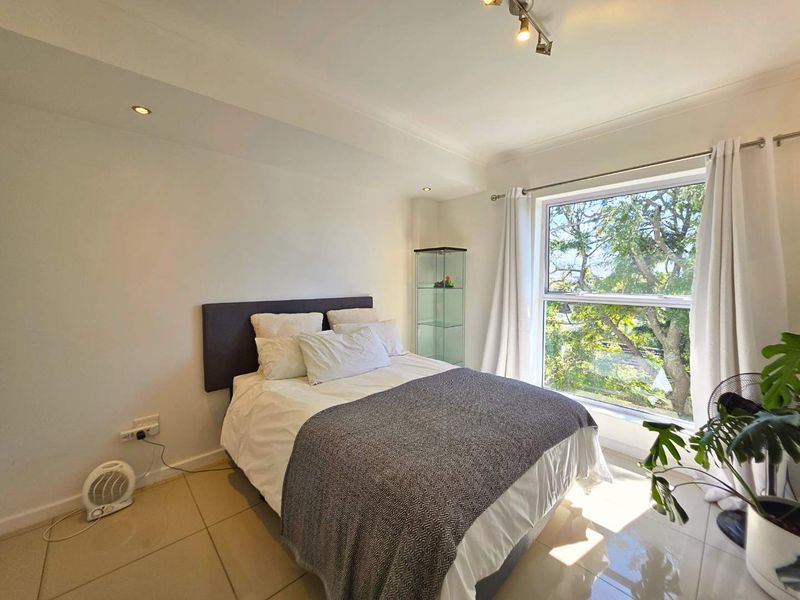 A bright bedroom featuring tiled flooring, recessed downlighting, and a large window providing natural light and pleasant outdoor views.