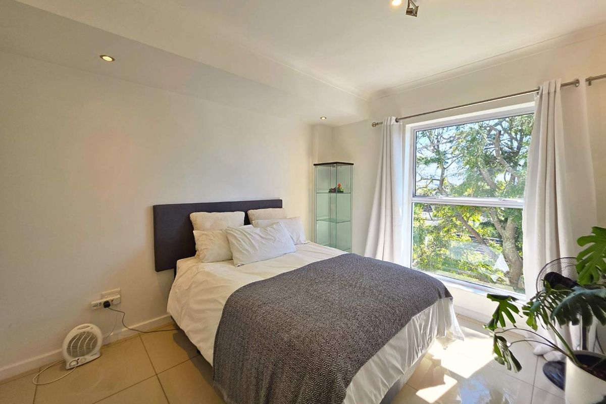 A bright bedroom featuring tiled flooring, recessed downlighting, and a large window providing natural light and pleasant outdoor views.