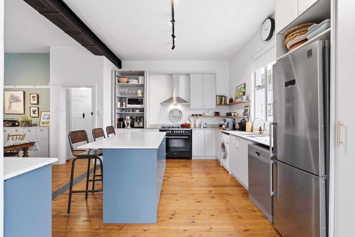 Modern kitchen featuring a central island with quartz countertops, hardwood flooring, stainless steel appliances, and ample built-in cabinetry under an exposed ceiling beam.