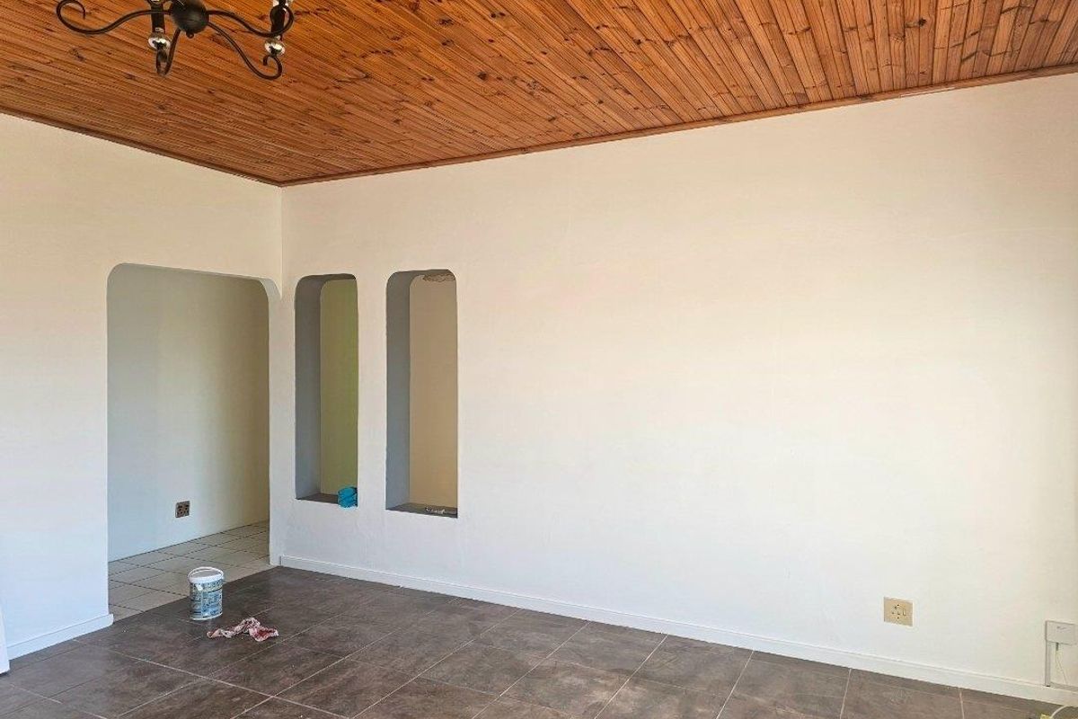 An empty living area featuring tiled flooring, a timber-clad ceiling, and decorative wall niches leading into an adjacent space.