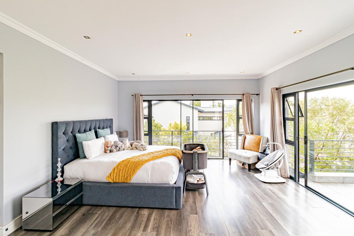 Spacious bedroom featuring modern wood-look flooring, recessed ceiling lighting, and large sliding glass doors opening onto a private balcony with scenic views.