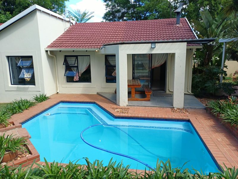 A well-maintained rear exterior featuring a swimming pool with brick coping, adjacent to a covered patio area with tiled flooring and security access.