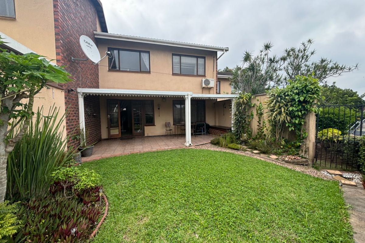 Rear view of the townhouse featuring a covered patio area, established garden, and brick and plaster facade with a satellite dish.