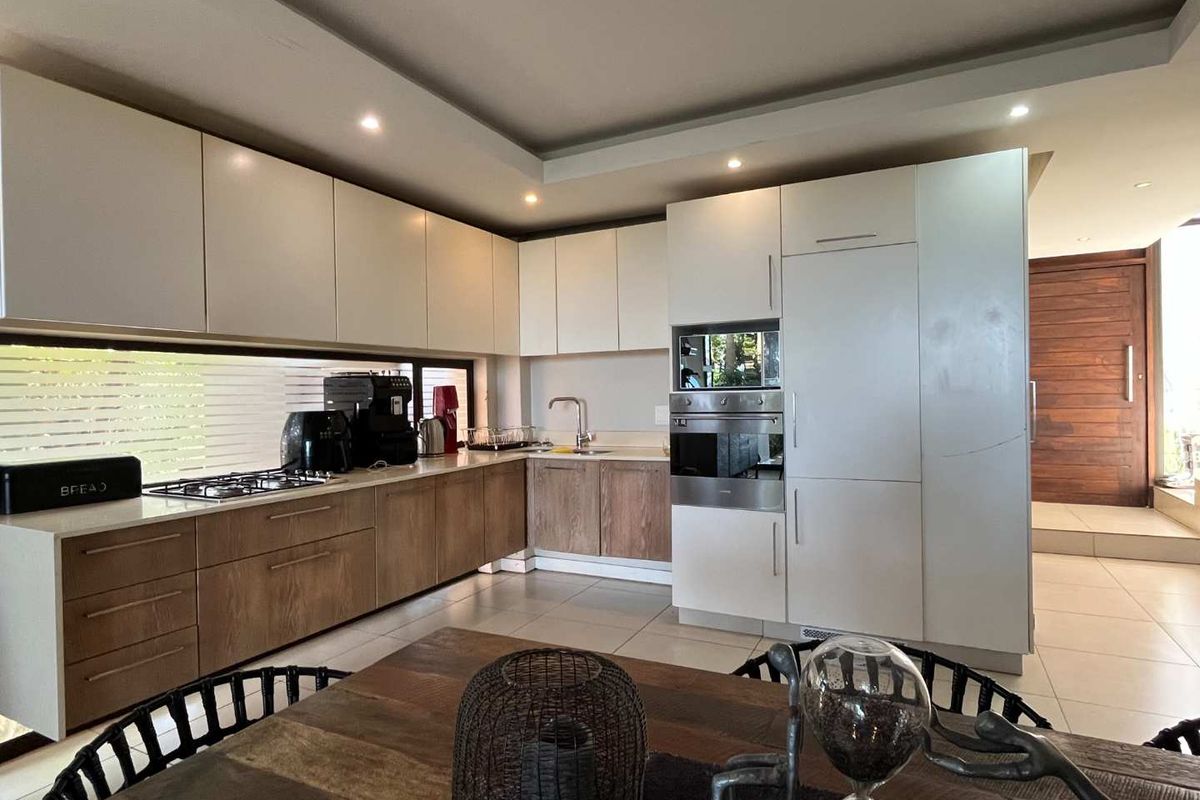 Modern kitchen featuring two-tone cabinetry, integrated oven and microwave, gas hob, and sleek stone countertops with a horizontal window splashback.