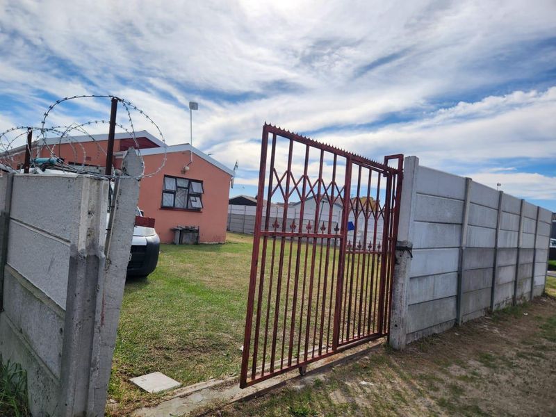 Front exterior view of the property featuring a gated entrance, precast concrete boundary wall with razor wire, and a small front yard area.