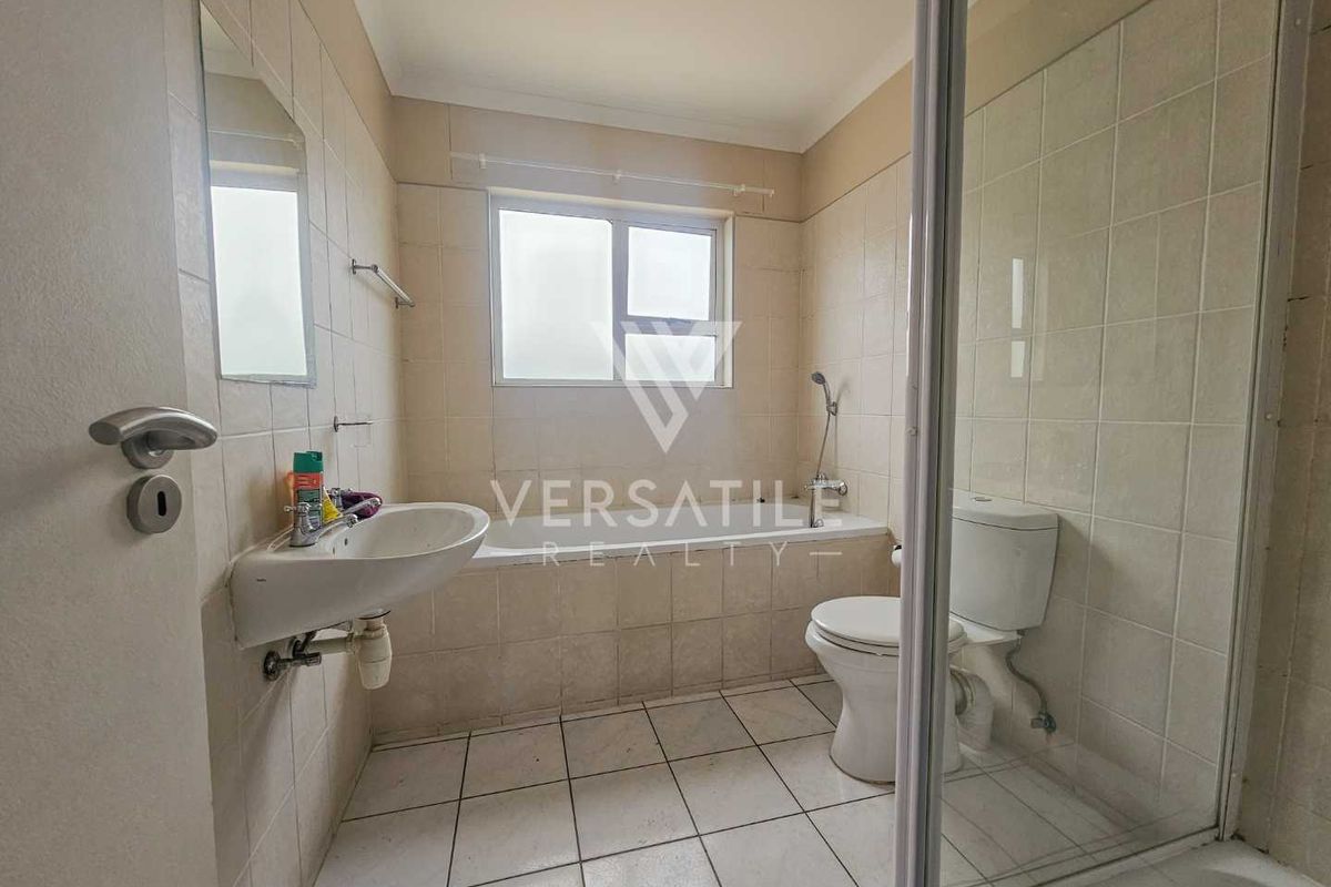 A functional bathroom featuring a shower enclosure, toilet, and wall-mounted basin with tiled walls and flooring.