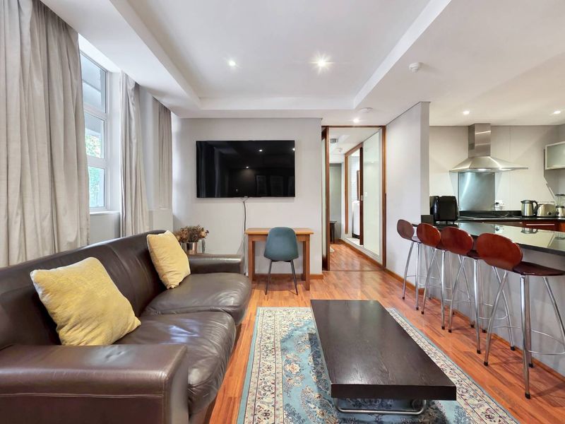 Modern open-plan living area featuring hardwood flooring, recessed lighting, and a sleek kitchen with granite countertops and stainless steel extractor fan.