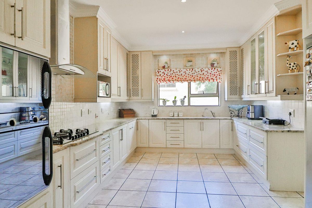 A well-maintained kitchen featuring light-toned cabinetry, granite countertops, a built-in oven, gas hob, and tiled flooring.