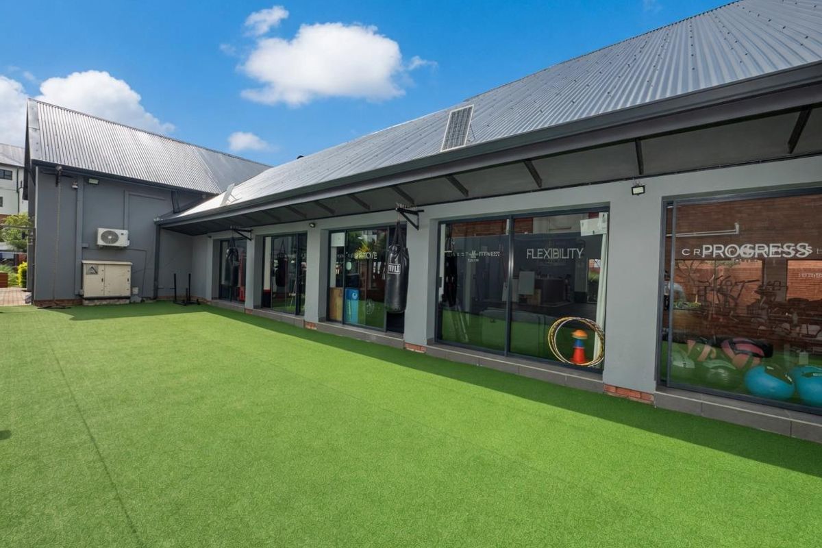 A well-maintained rear exterior area featuring artificial turf, large sliding glass doors, and a modern metal roof structure.