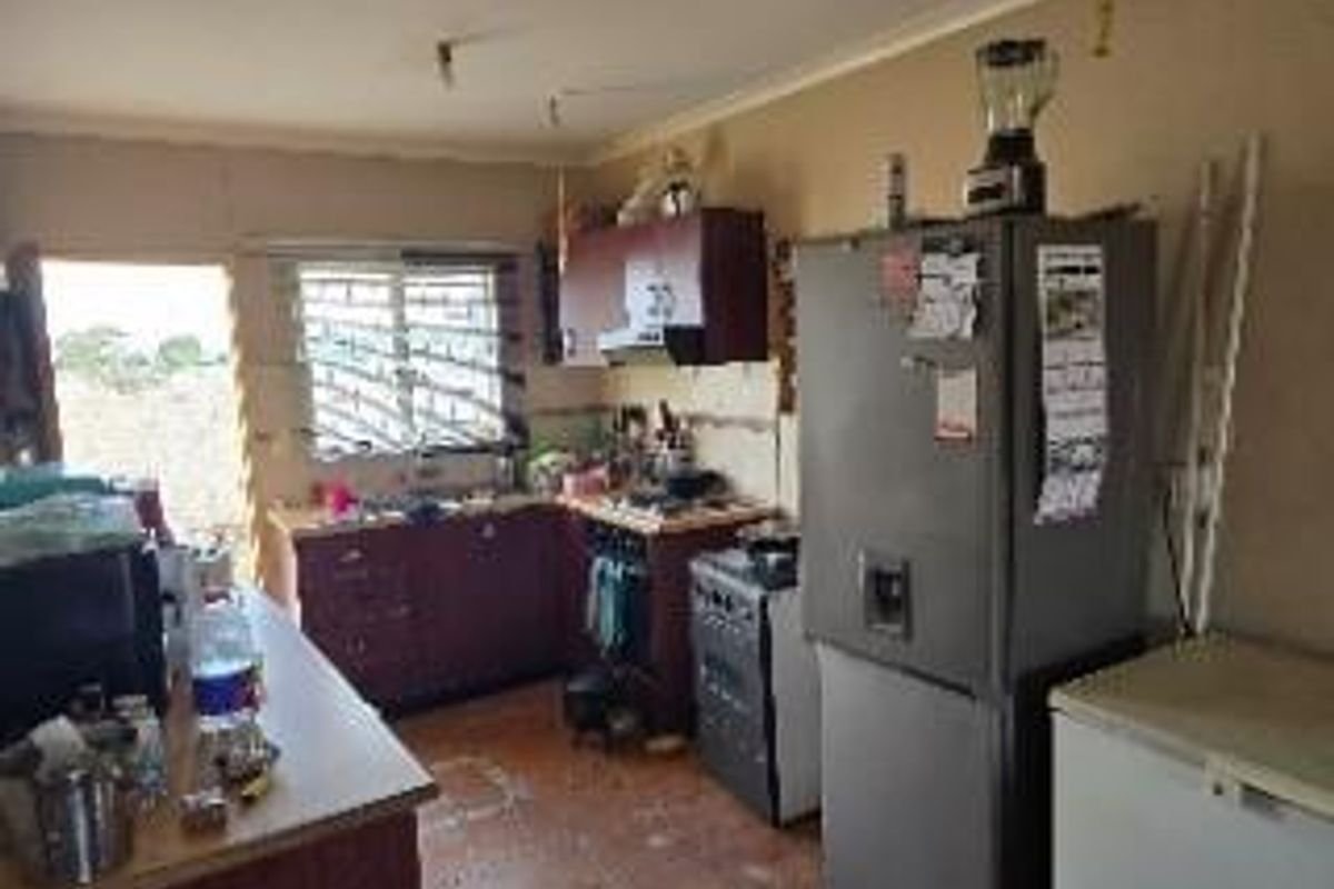 A dated kitchen featuring dark cabinetry, tiled flooring, and a functional layout with built-in stove and extractor fan.