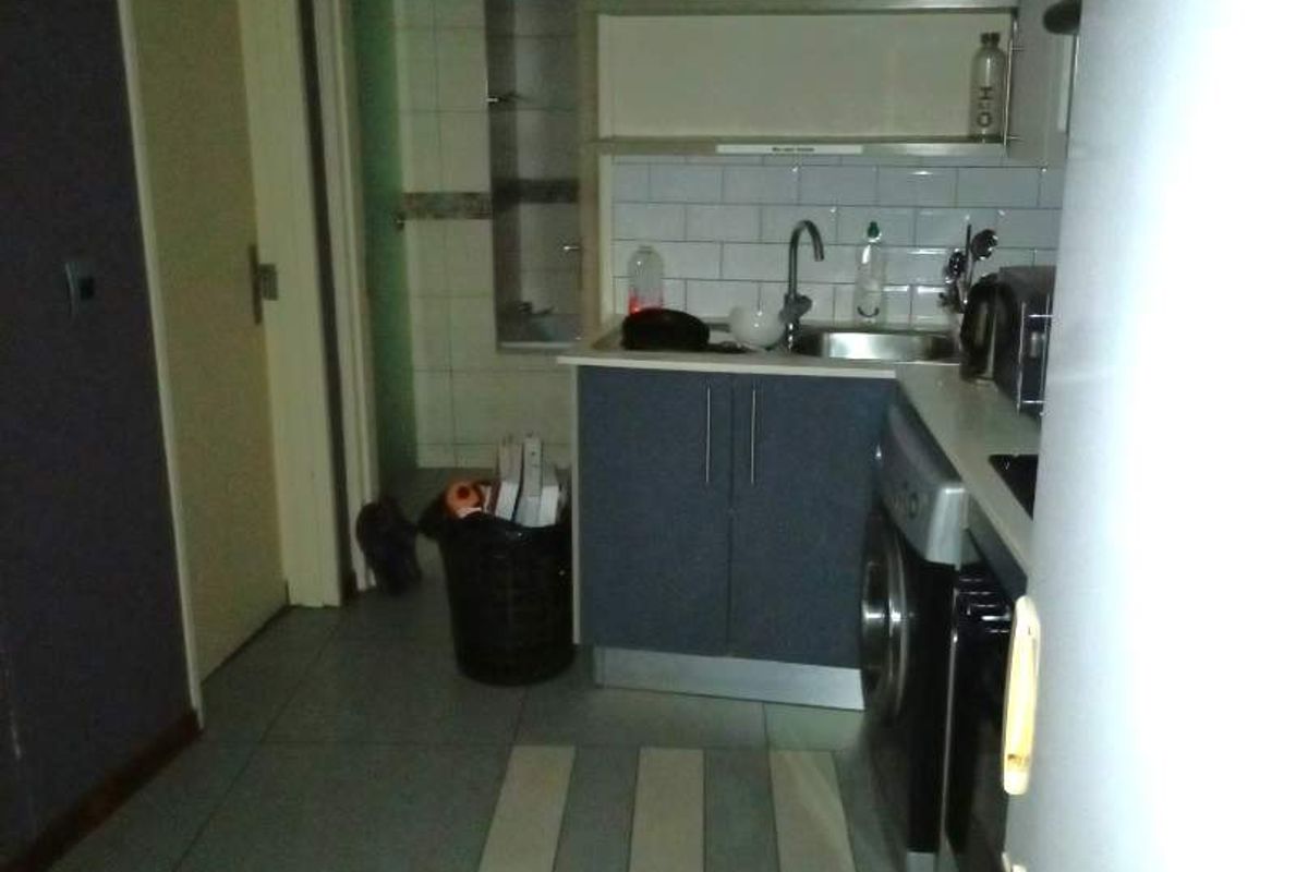 A compact kitchen area featuring built-in cabinetry, a tiled backsplash, and open shelving, requiring cosmetic updates to improve its overall aesthetic and functionality.