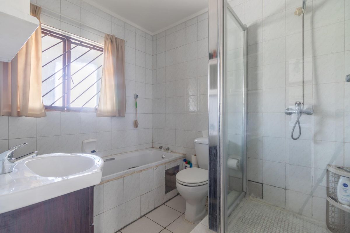 A functional bathroom featuring a built-in bathtub, separate glass-enclosed shower, vanity basin, and toilet, finished with full-height wall tiling.