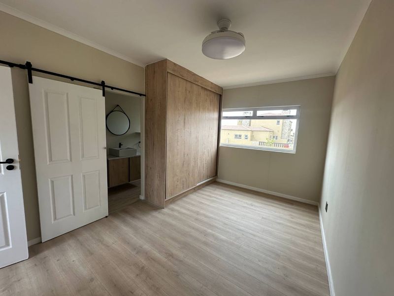 A bright, empty bedroom featuring modern laminate flooring, a large built-in wardrobe, and a sliding barn door leading to an en-suite bathroom.