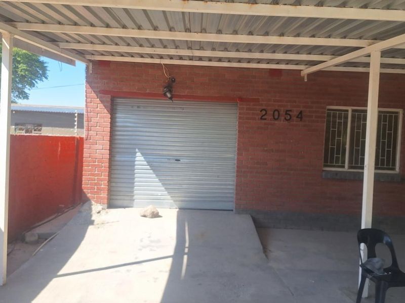 A single garage with a roller shutter door, brick exterior, and a covered carport area.