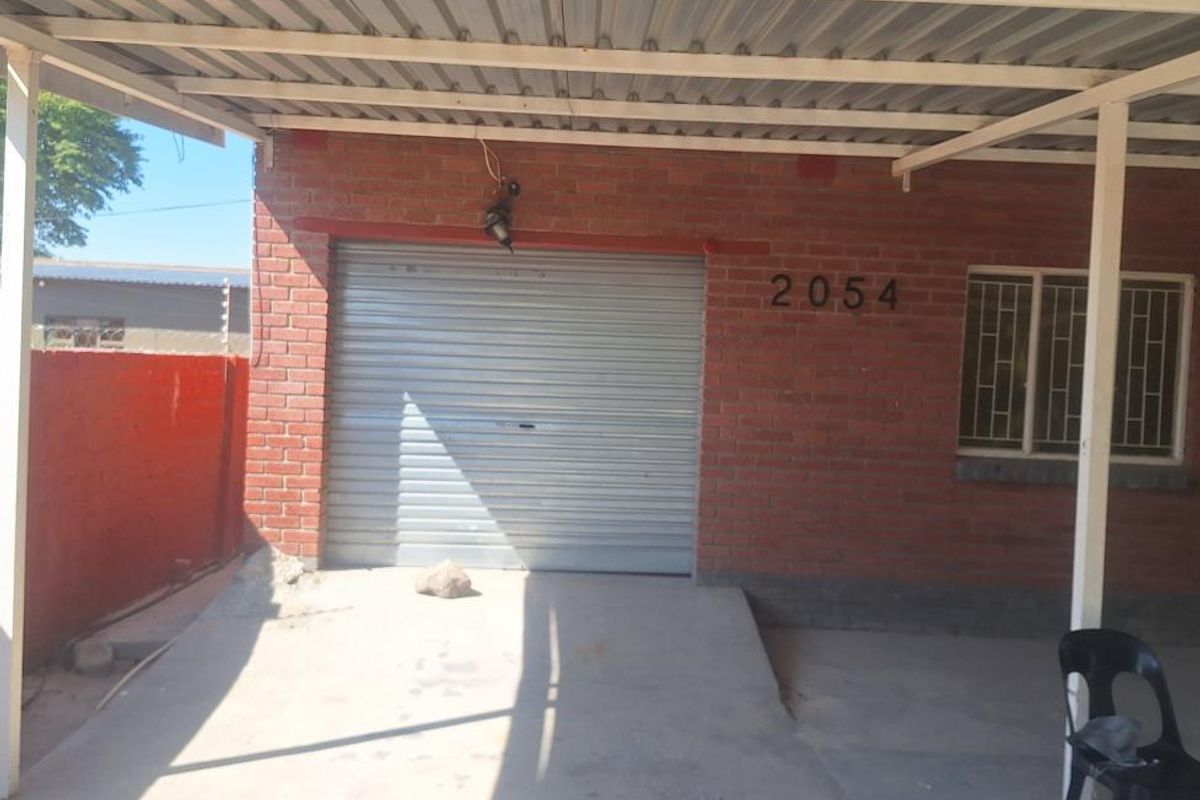 A single garage with a roller shutter door, brick exterior, and a covered carport area.