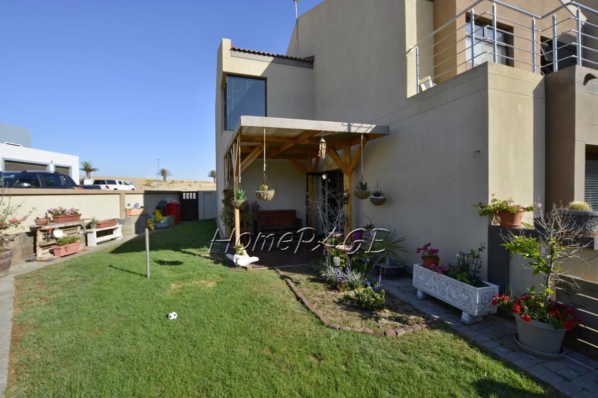 Rear view of the townhouse featuring a private garden, a timber-framed patio cover, and an upper-level balcony with metal railings.