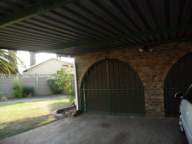 A covered carport area featuring arched metal security gates, brick masonry, and a corrugated metal roof, providing secure parking space.