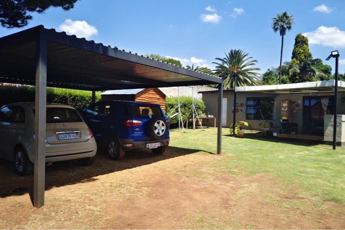 A spacious rear garden featuring a large metal carport, a paved patio area, and well-maintained lawn space.