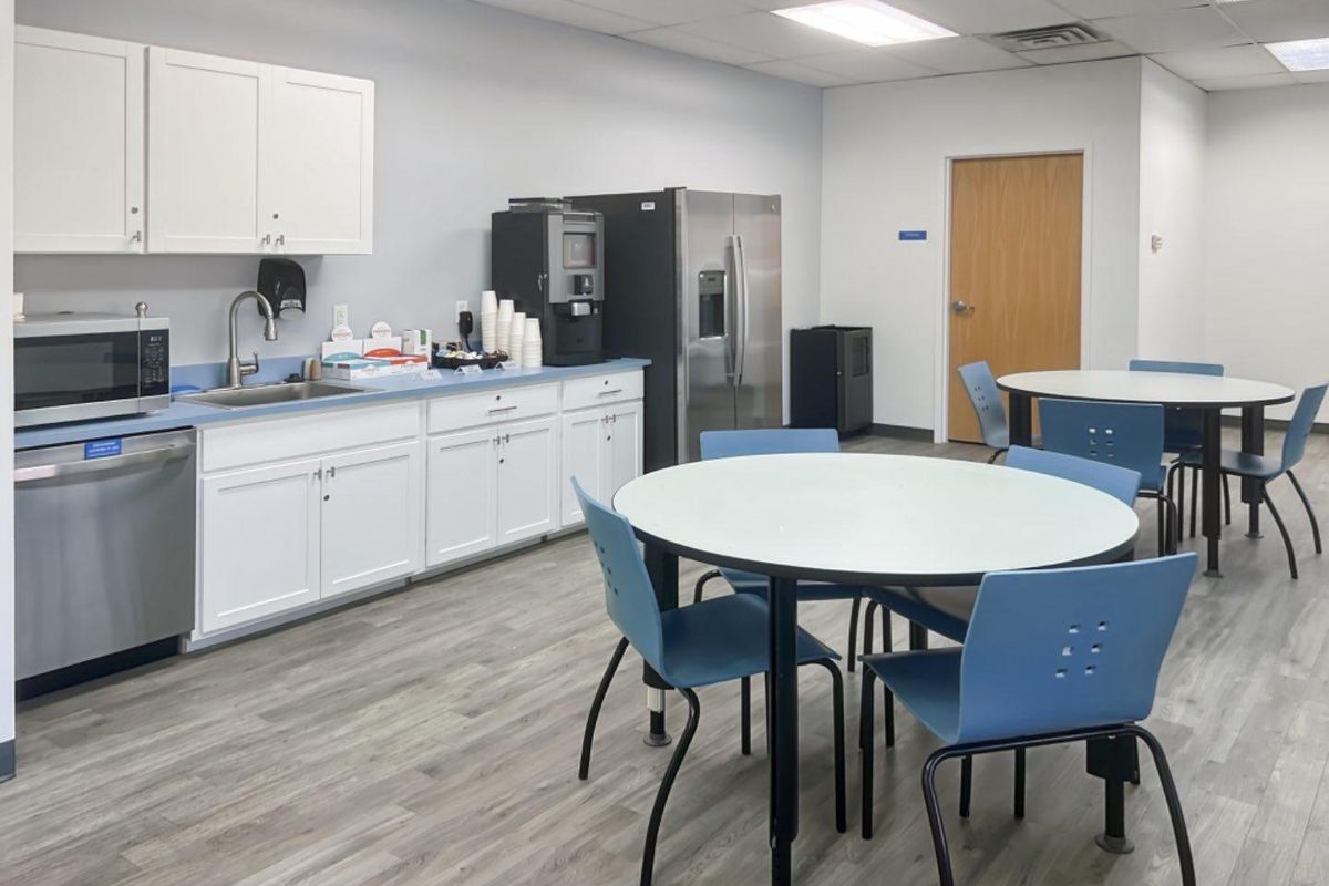 A functional office breakroom featuring white cabinetry, stainless steel appliances, a sink, and durable laminate flooring with a drop ceiling.