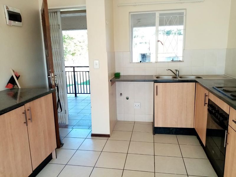 Functional kitchen featuring laminate cabinetry, built-in oven, hob, double bowl sink, and tiled flooring, with direct access to an outdoor balcony area.