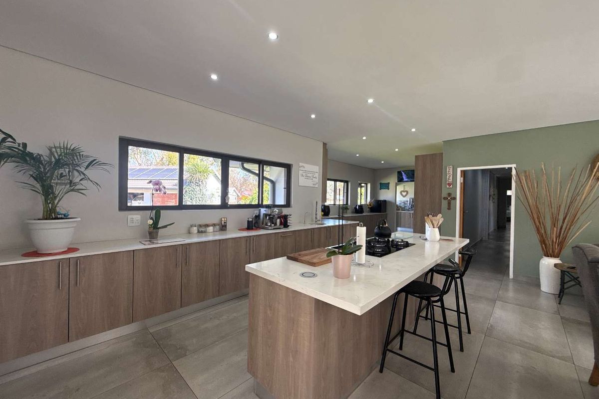 Modern open-plan kitchen featuring wood-grain cabinetry, stone countertops, a central island with a built-in hob, and large-format floor tiles.