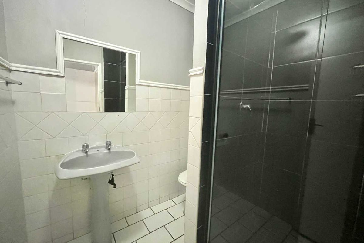 A functional bathroom featuring a pedestal basin, wall-mounted mirror, and a glass-enclosed shower with tiled walls and flooring.
