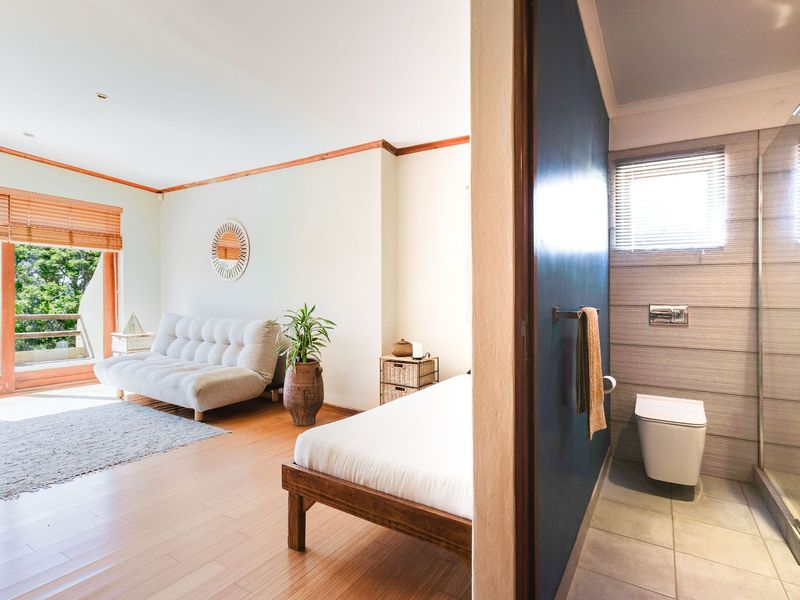 An open-plan living area featuring laminate flooring and a modern en-suite bathroom with a glass shower enclosure and wall-mounted toilet.