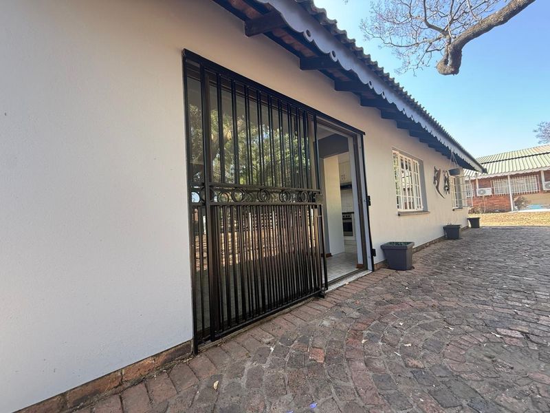 Rear exterior view of the cottage featuring a paved patio area, security gate, and sliding door access to the interior.