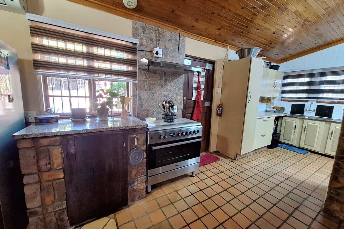 A rustic kitchen featuring a stainless steel oven, extractor fan, granite countertops, brick-base cabinetry, and tiled flooring under a timber-paneled ceiling.