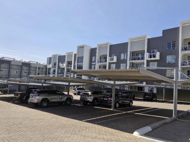 Exterior view of a modern apartment complex featuring covered parking bays and private balconies.
