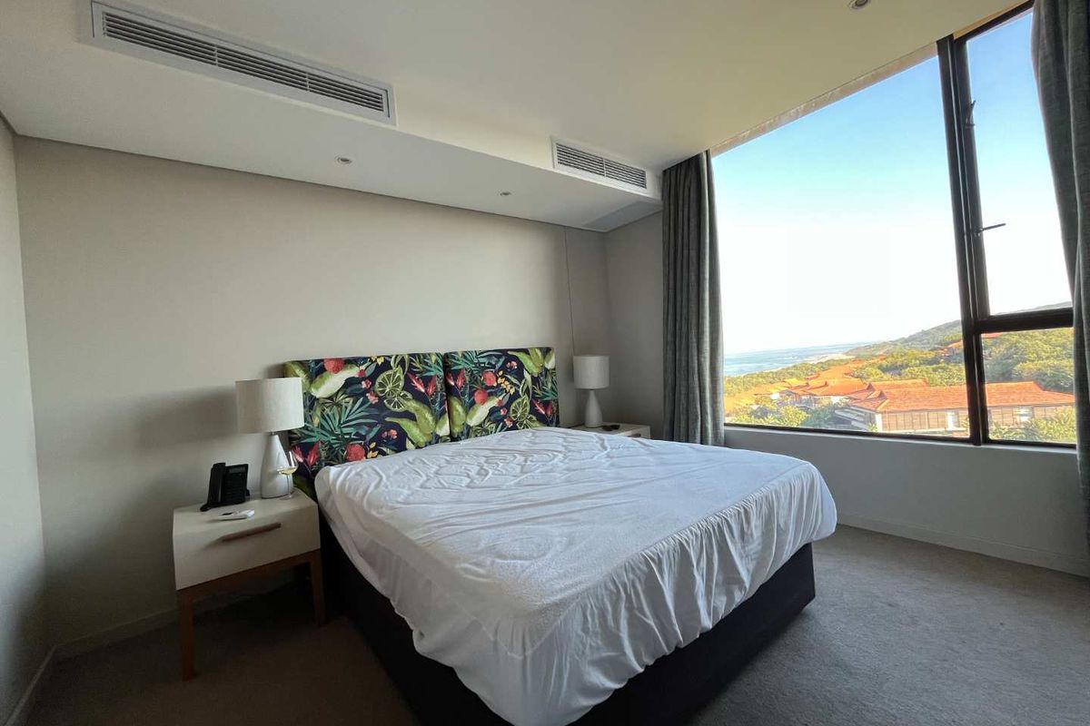 A bright bedroom featuring floor-to-ceiling windows with scenic coastal views, integrated ceiling air conditioning, and neutral carpeting.