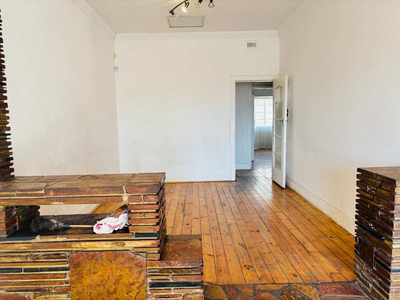 An empty living room featuring original hardwood flooring and a prominent stone fireplace, leading through to an adjacent room.