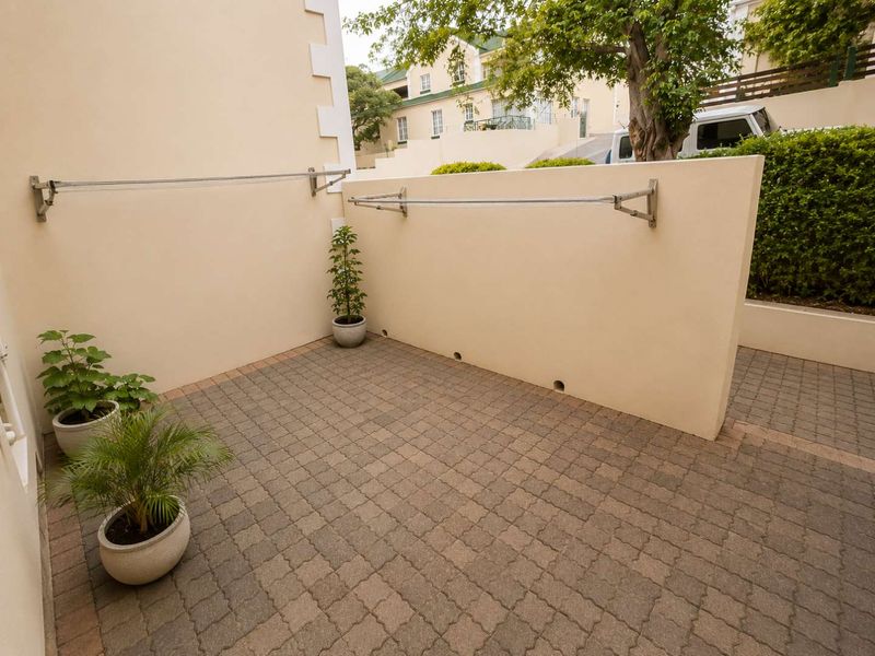 A private paved rear courtyard featuring a wall-mounted clothesline and low retaining wall, providing a functional outdoor utility space.
