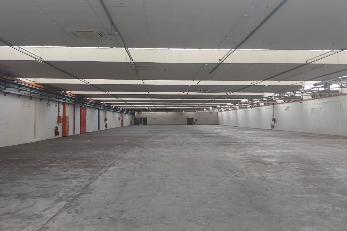 Expansive industrial warehouse space featuring high ceilings, durable concrete flooring, and large access doors, suitable for storage or manufacturing operations.