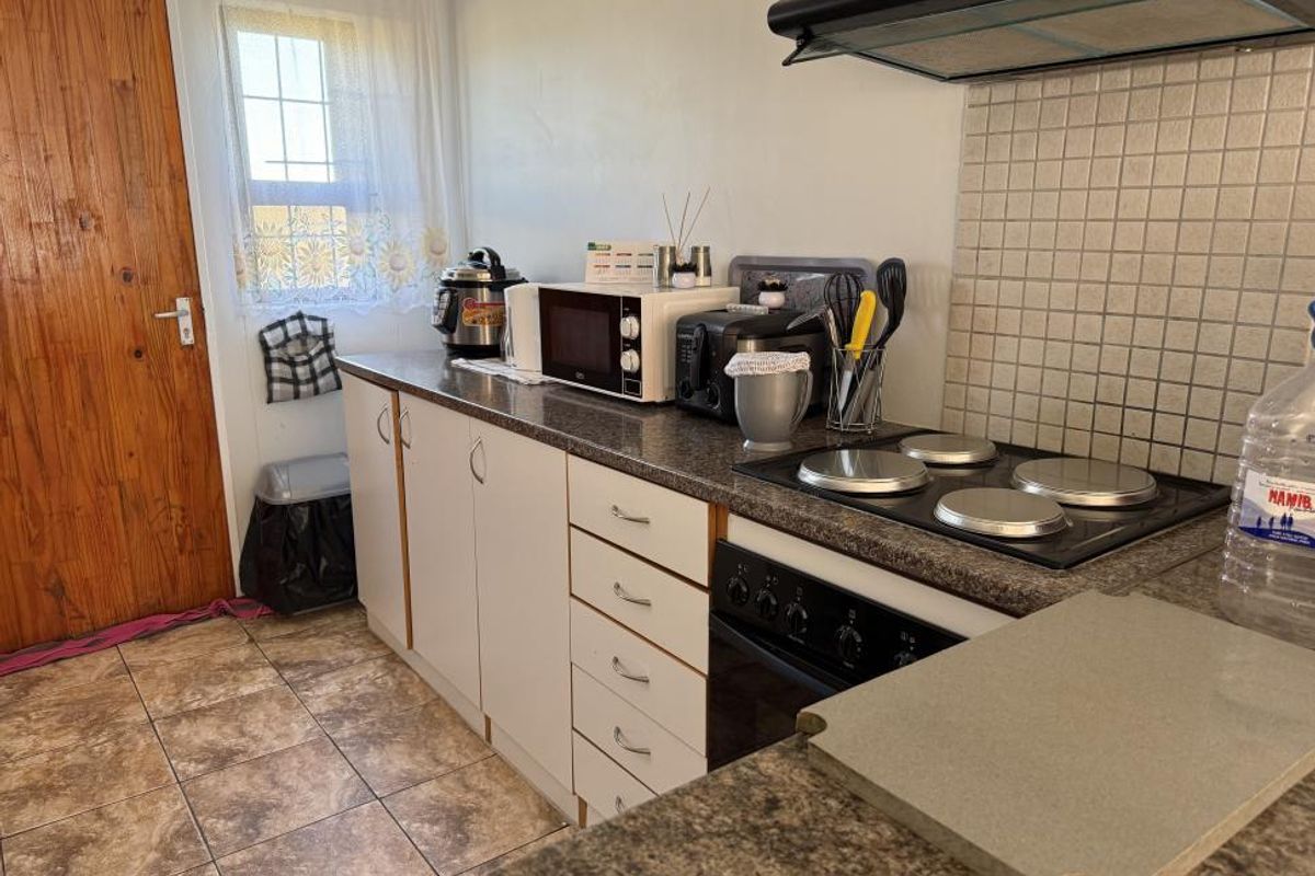 A functional kitchen featuring built-in cabinetry, laminate countertops, an electric hob with extractor fan, and tiled flooring.
