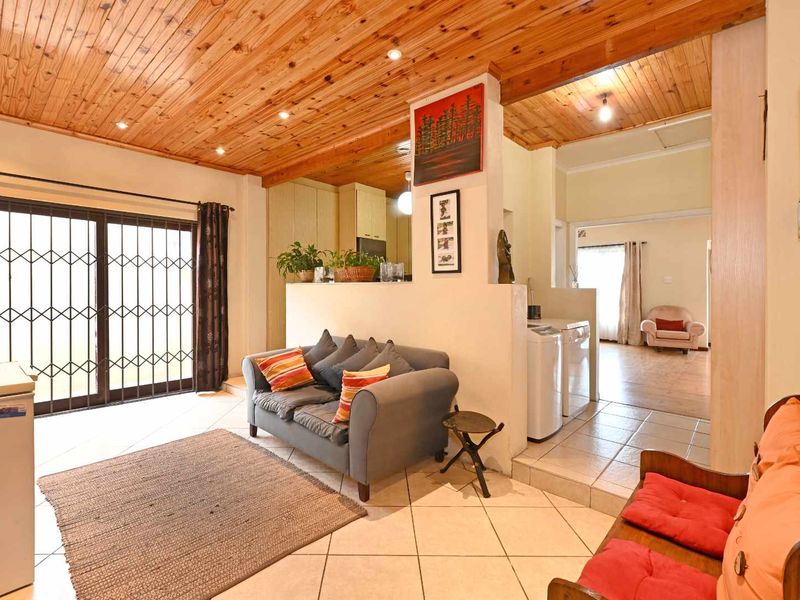 Open-plan living area featuring a distinctive timber-clad ceiling, tiled flooring, and a partition wall separating the living space from the laundry and hallway areas.