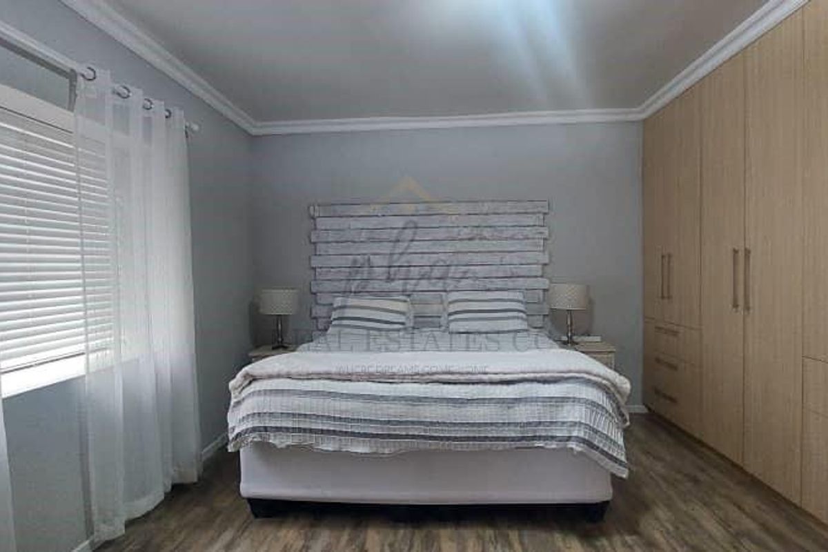 A well-maintained bedroom featuring extensive built-in wooden cupboards, laminate flooring, and neutral wall finishes, providing ample storage and a clean aesthetic.