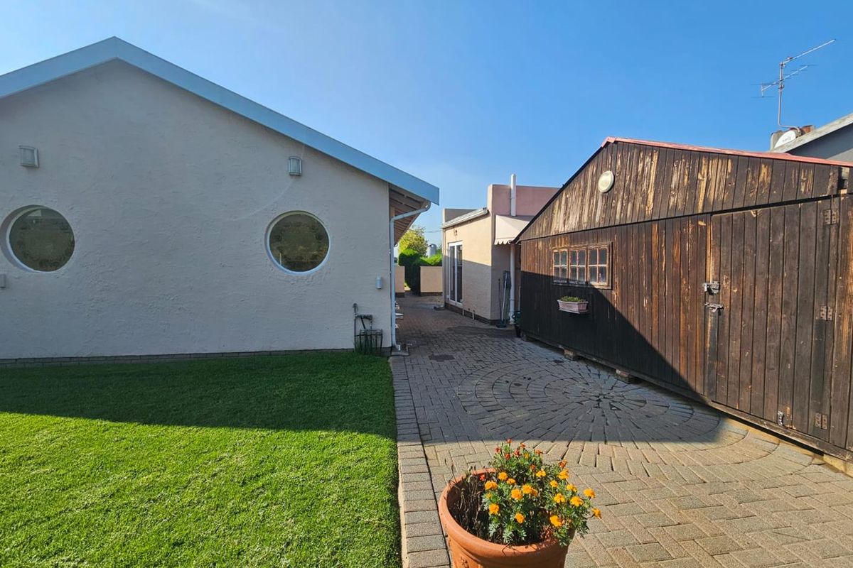 Exterior view showing a paved courtyard area between the main dwelling and a timber-clad garage structure with a manicured lawn.