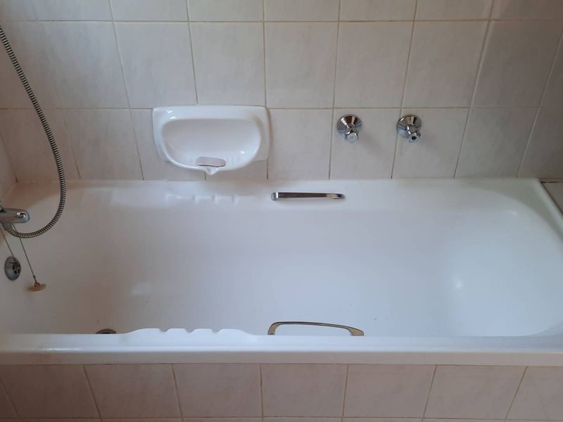 A functional bathroom featuring a built-in bathtub with chrome fixtures and tiled surround, presenting a clean but dated aesthetic.