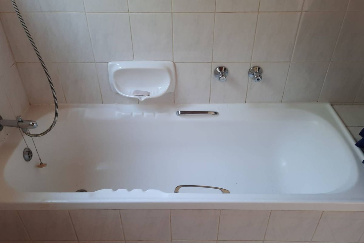 A functional bathroom featuring a built-in bathtub with chrome fixtures and tiled surround, presenting a clean but dated aesthetic.