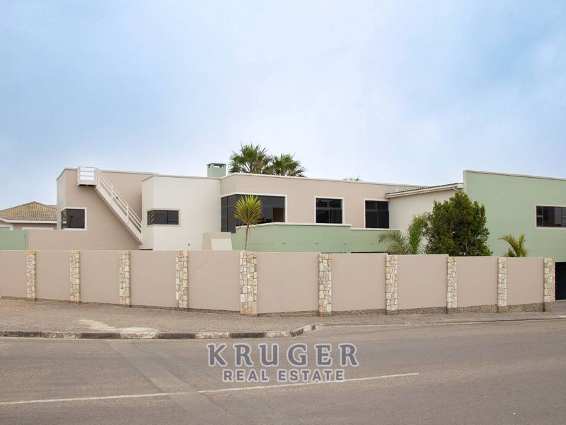 A modern multi-level residential property featuring a secure boundary wall with stone-clad pillars and an external staircase, situated on a corner lot.