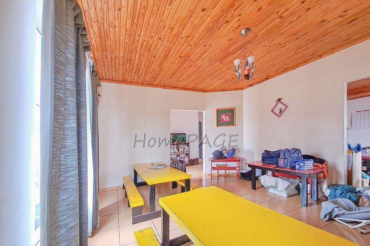 A living area featuring a timber-clad ceiling, tiled flooring, and direct access to an adjacent room.