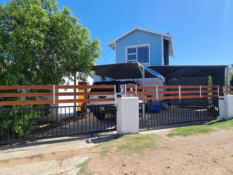 Front exterior view of the property featuring a timber and metal slat fence, sliding gate, concrete driveway, and a shade cloth carport.
