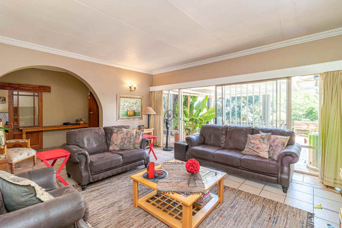 Spacious living room featuring large sliding glass doors that open to a covered patio, arched entryway, and neutral tiled flooring.