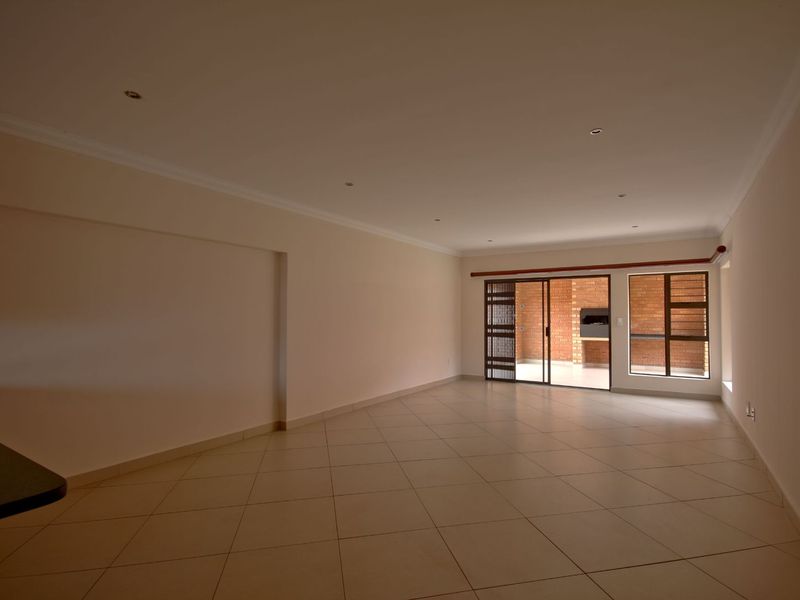Spacious open-plan living area featuring tiled floors, recessed lighting, and seamless access to an outdoor patio with a built-in braai.
