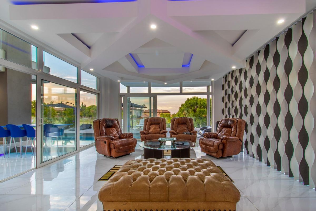 Modern living room featuring a unique geometric coffered ceiling with integrated LED lighting, large floor-to-ceiling glass sliding doors, and polished porcelain tile flooring.